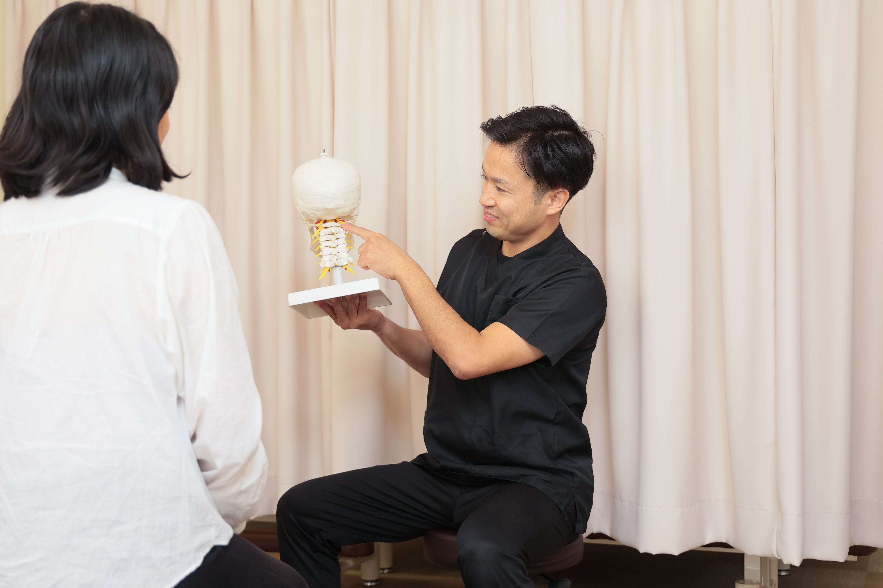 脊椎模型を使いながら腰の骨のずれの原因をわかりやすく説明する院長